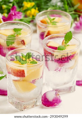 Fresh sparkling beverage with peaches and ice with rose petals on white wooden background, selective focus
