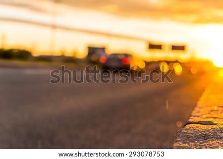 Sunset in the city. View of the flow of cars racing down the highway from the level of the pavement, focus on the border
