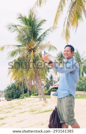 Men traveler with backpack using mobile phone at the beach 