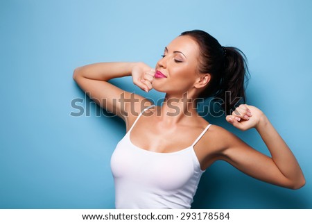Attractive healthy woman is exercising in morning. Her eyes are closed with pleasure.  She is smiling. Isolated on blue background