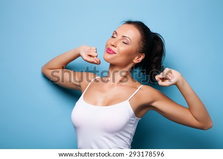 Cheerful girl is stretching her arms after sleeping. She closed her eyes happily and smiling. Isolated on blue background