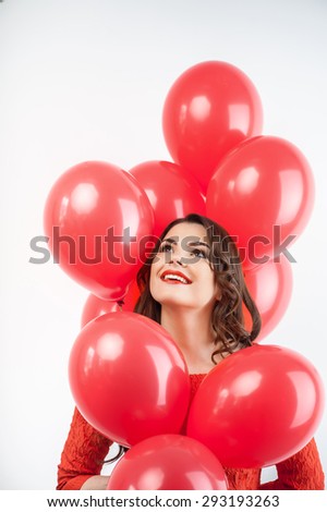 Pretty woman is holding balloons and looking up dreamingly. She is smiling. Isolated on grey background
