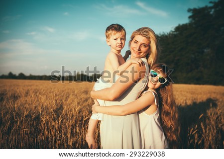 Young happy beautiful mother , daughter and son . Mother with children goes on field.  Happy family. Expressing emotions of joy, freedom, success. Silhouettes on sunny sky