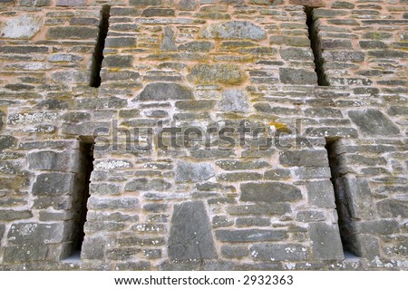 Looking up a traditional old medieval stone wall with four arrow windows.