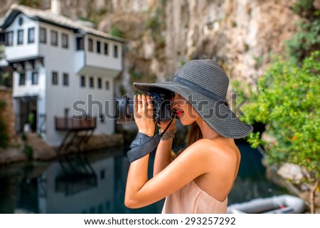 Young woman in pink dress and hat photographing house in Blagaj village in Bosnia and Herzegovina