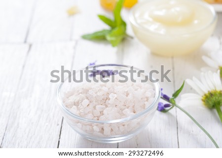 cosmetic creams, lip balm, soap and bath salt with herbal flowers on white wooden table 