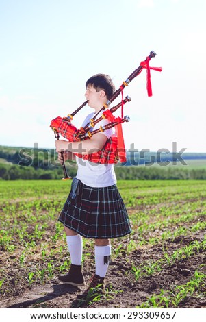 Picture of man enjoying playing pipes in Scottish traditional kilt on green outdoors copy space summer field background