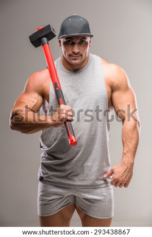 Muscular bodybuilder with hammer on gray background.