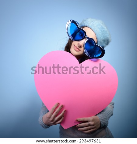 Cute attractive girl posing with big pink heart over blue background. Holiday