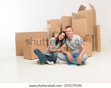 young happy couple sitting on floor in new apartment with moving boxes in background