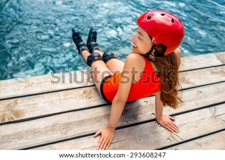Young woman in red sportswear with skating rollers resting on the wooden pier near the sea
