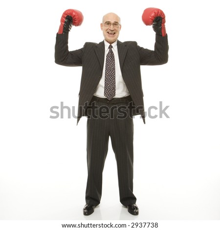Smiling Caucasian middle-aged businessman standing with arms raised wearing boxing gloves.