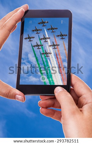 a woman using a smart phone to take a photo of an airshow performance