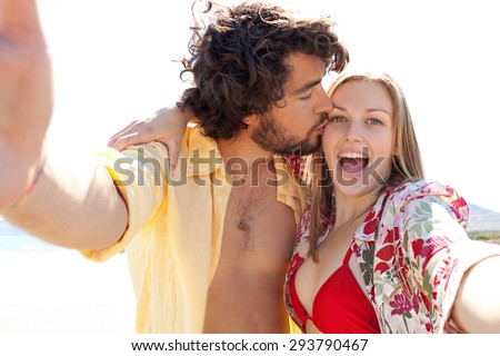 Portrait of tourist couple using technology to take selfies pictures of themselves pulling faces, enjoying a summer holiday together on a beach on vacation, outdoors. Travel and technology lifestyle.