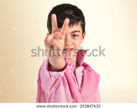 Child doing victory gesture over ocher background 