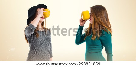 Twin girls drinking coffee over ocher background