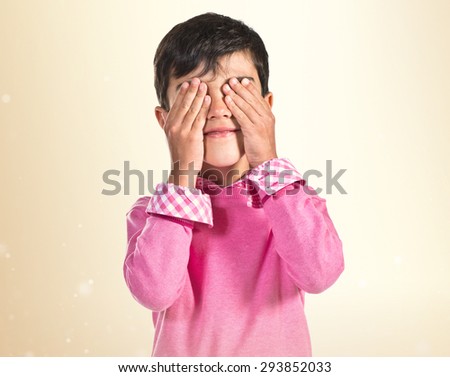 Kid covering his eyes over ocher background