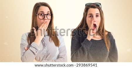 Twin sisters doing surprise gesture over ocher background