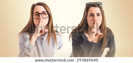 Twin sisters making silence gesture over ocher background
