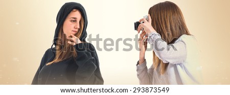 Girl photographing at her twin sister over ocher background