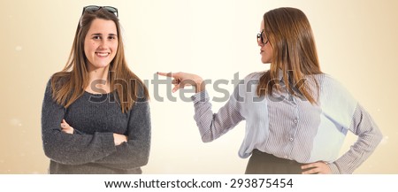 Pretty girl presenting her twin sister over ocher background  