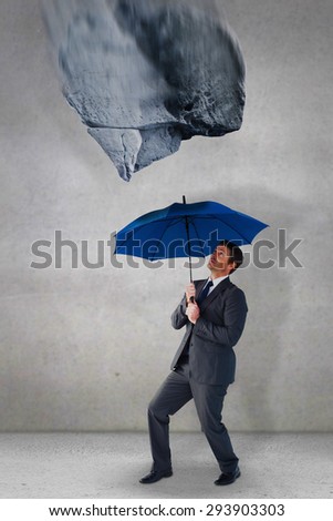 Businessman sheltering under blue umbrella against grey room