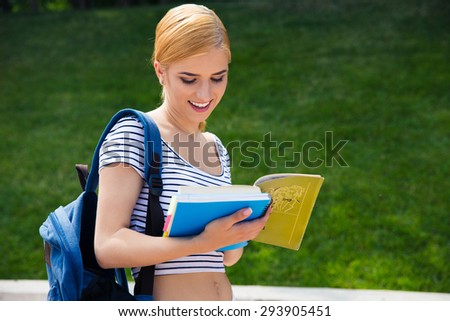 Happy female student reading book outdoors