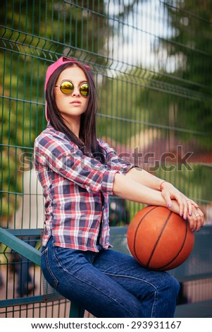Outdoor lifestyle portrait of pretty young sitting girl, wearing in hipster swag grunge style with basketball urban background. Retro vintage toned image, film simulation.