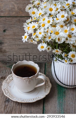 Tea cup and flowers in a pot on a vintage wooden background