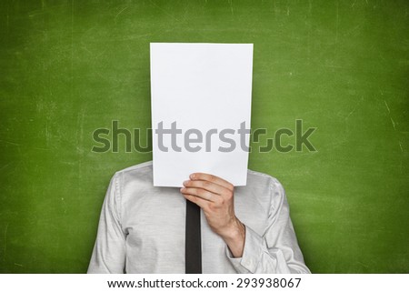 Businessman holding empty paper sheet front of head on blackboard background