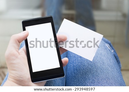 Hand holding a visit card with white blank and smartphone with jeans background. Mock-up Photo of business cards. Template for branding identity on dark background. 