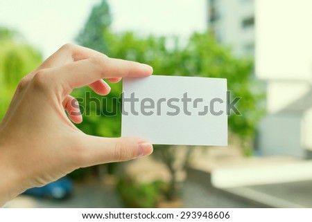 Hand holding a white business card on blurred trees background. Mock-up Photo of business cards. Template for branding identity on dark background.