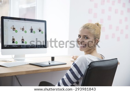 Smiling female photo editor sitting at the table in office and looking at camera