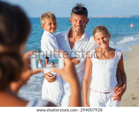 Mother taking family picture with father and two children at the tropical beach. Focus on the family