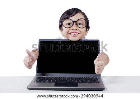 Cute little girl showing two thumbs up on the camera with empty laptop screen on desk, isolated on white