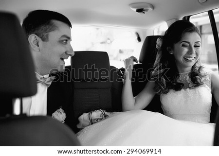 Cute happy smiling bride with the groom are sitting on the back seat of car