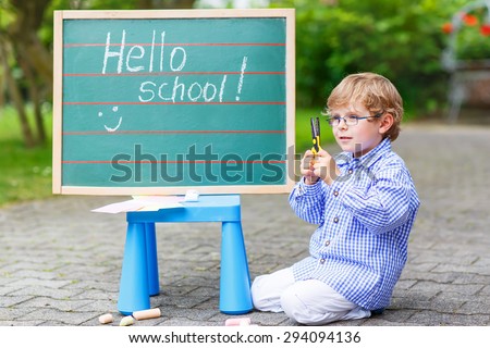 Cute preschool kid boy with glasses at blackboard practicing writing, outdoor. school or nursery. Back to school concept