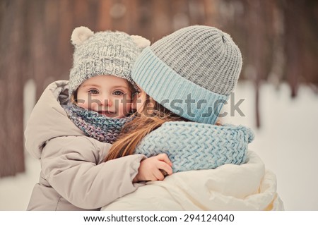 happy mother holding baby girl on the walk in winter snowy forest