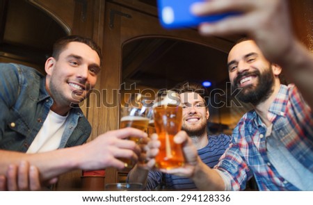 people, leisure, friendship, technology and bachelor party concept - happy male friends with smartphone taking selfie and drinking beer at bar or pub