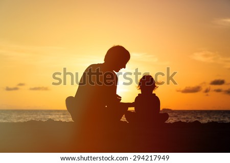Silhouette of father and little daughter on sunset beach