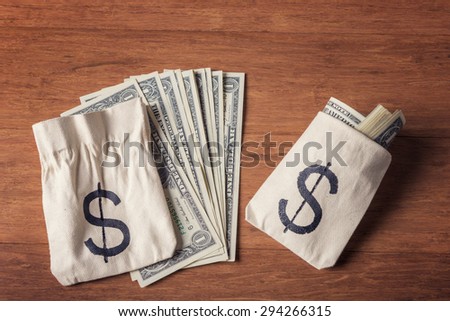 Dollar bills with money bags over wooden background