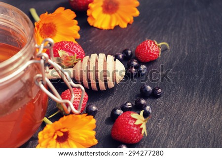 Honey glass,wooden dipper,berries, calendula on dark background