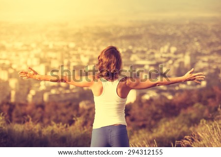 Young woman spreading hands wide open with city on background. Freedom concept. Love and emotions, woman happiness. Toned image
