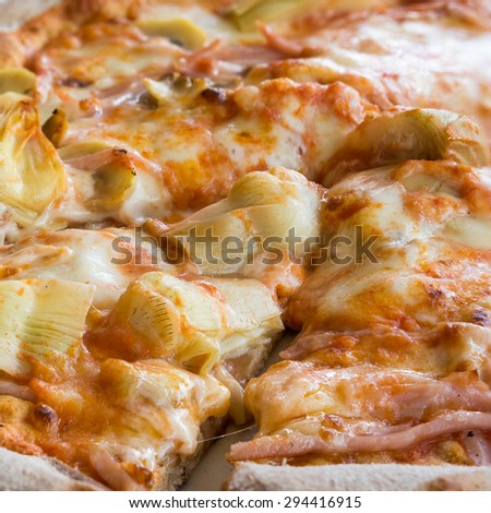 In the picture a cut pizza with tomato, mozzarella, mushrooms, ham and artichokes.