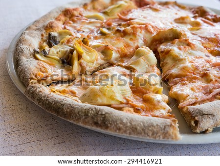 In the pictured a cut pizza with tomato, mozzarella, mushrooms, ham and artichokes.