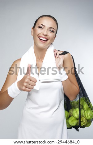 Portrait of Happy Professional Female Tennis Player With Mesh Bag of Balls Against White. Showing Thumbs Up Sign. Vertical Image