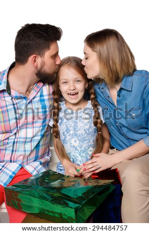 Happy family with shopping bags sitting at studio, isolated on white background. The parents kissing the girl. girl is laughing