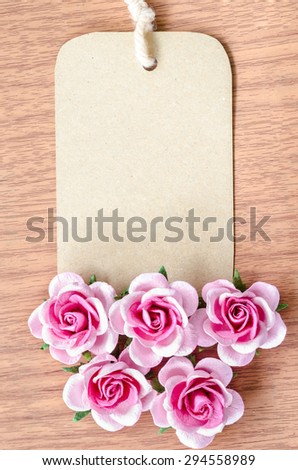 Brown paper tag and pink rose on wooden background for your text.