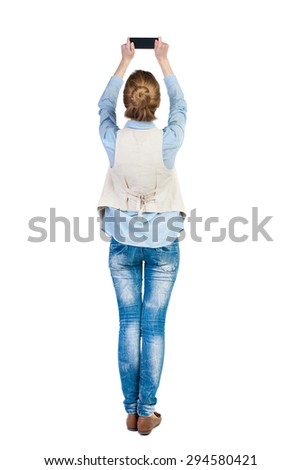 back view standing young beautiful  woman  in vest and using a mobile phone. girl  watching.  backside view person.  Isolated over white background. Girl in sleeveless photographs on top phone itself