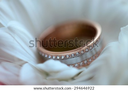 One golden wedding ring with diamonds on white fresh flower closeup, horizontal picture